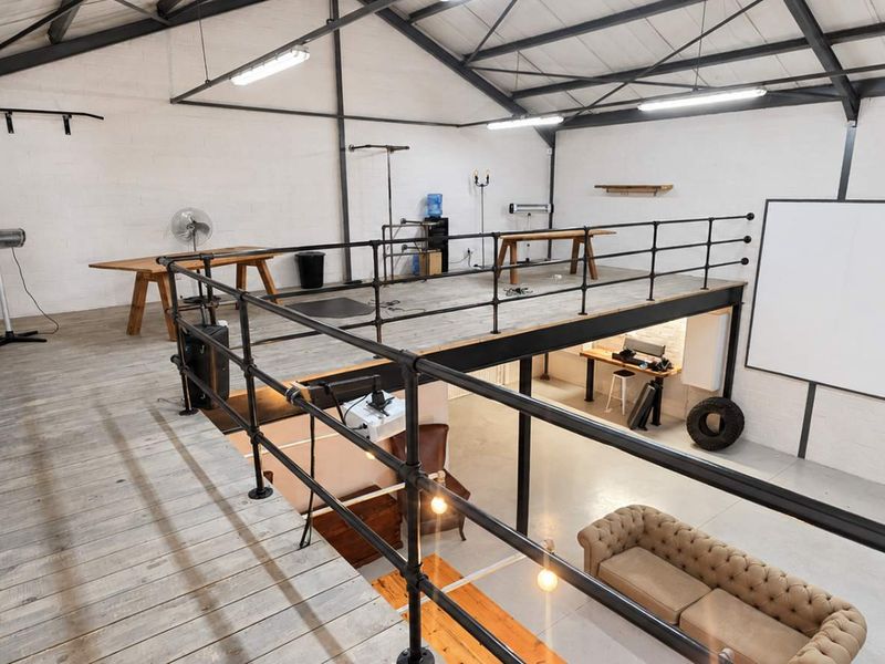 Spacious industrial open-plan unit featuring a mezzanine level, exposed steel roof trusses, painted brick walls, and a combination of timber and concrete flooring.