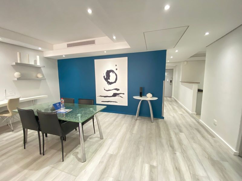 Modern dining area featuring light wood-look laminate flooring, recessed downlighting, and a striking blue accent wall with built-in shelving.