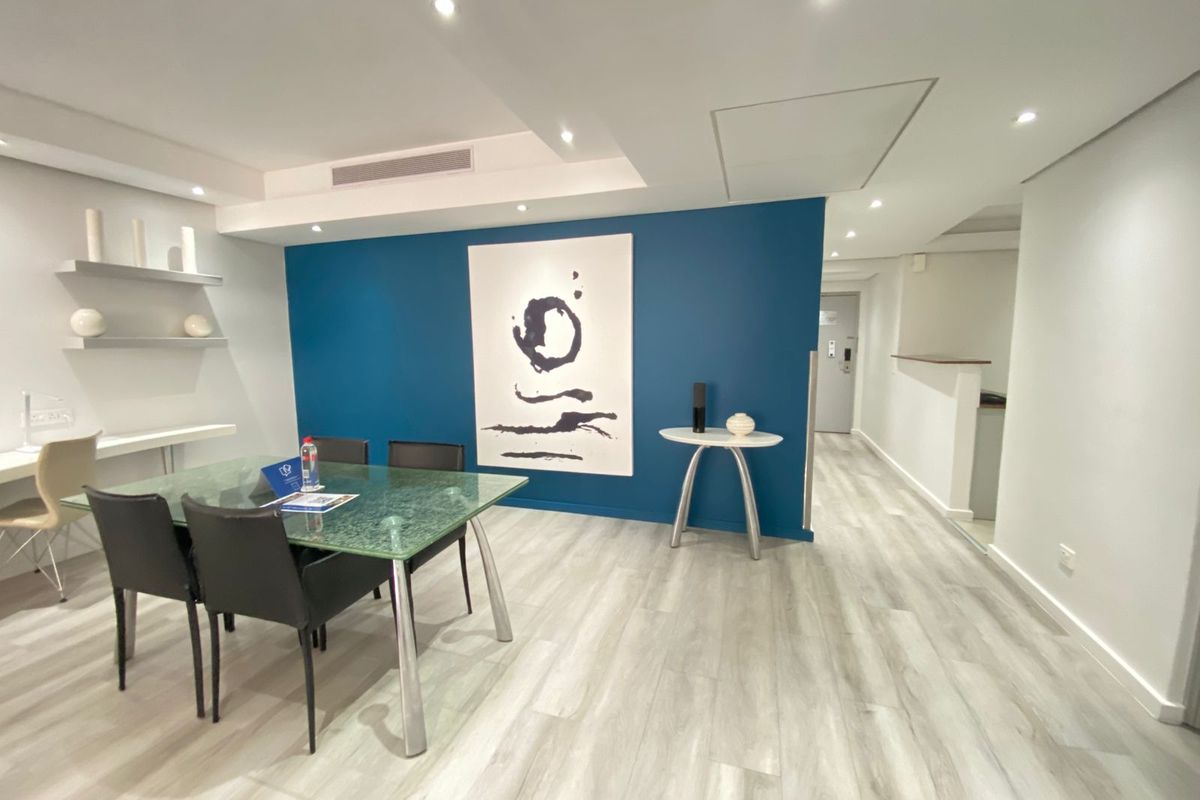 Modern dining area featuring light wood-look laminate flooring, recessed downlighting, and a striking blue accent wall with built-in shelving.