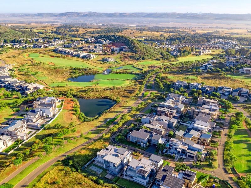 An aerial view of a residential estate featuring modern homes, landscaped green spaces, golf course fairways, and scenic lakes.