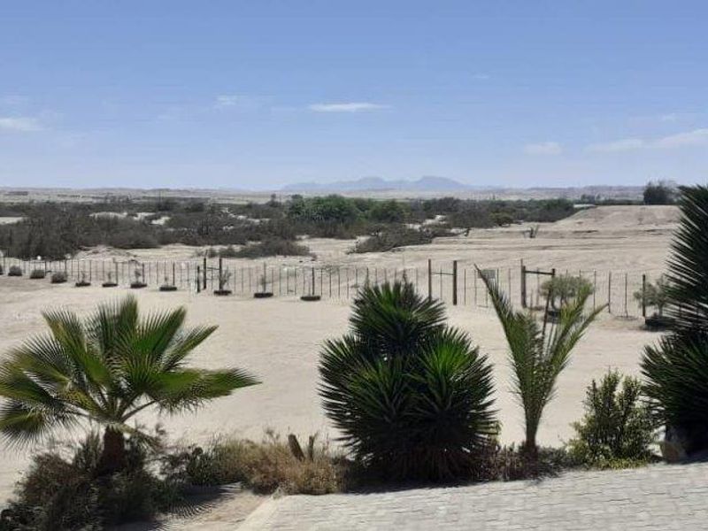 Expansive view of the surrounding arid landscape and desert terrain, featuring a paved foreground area and perimeter fencing.