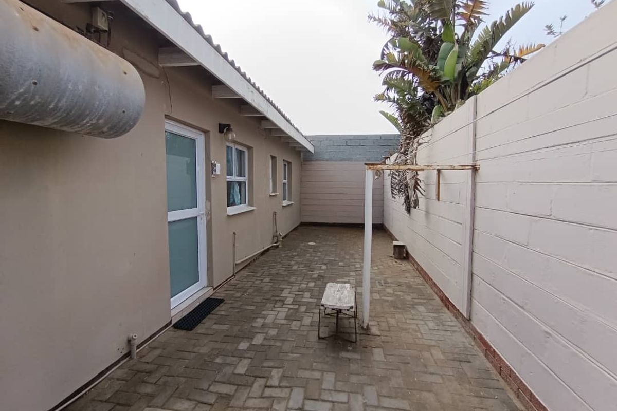 A narrow paved side yard area featuring a wall-mounted exterior water heater, a fixed washing line, and access to the main dwelling via a door.