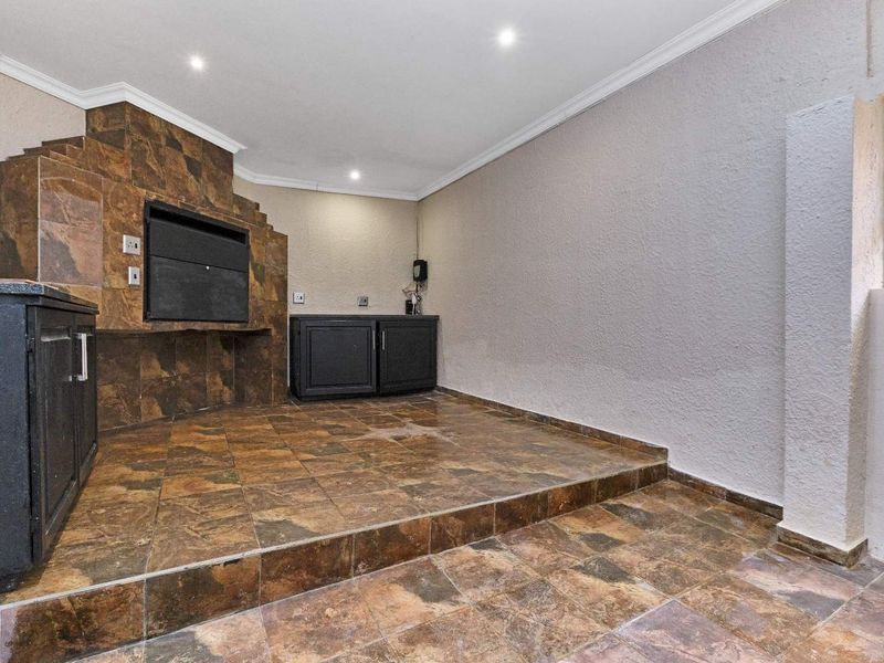 An empty covered patio area featuring a built-in braai, tiled flooring, and built-in cabinetry, suitable for outdoor entertaining.