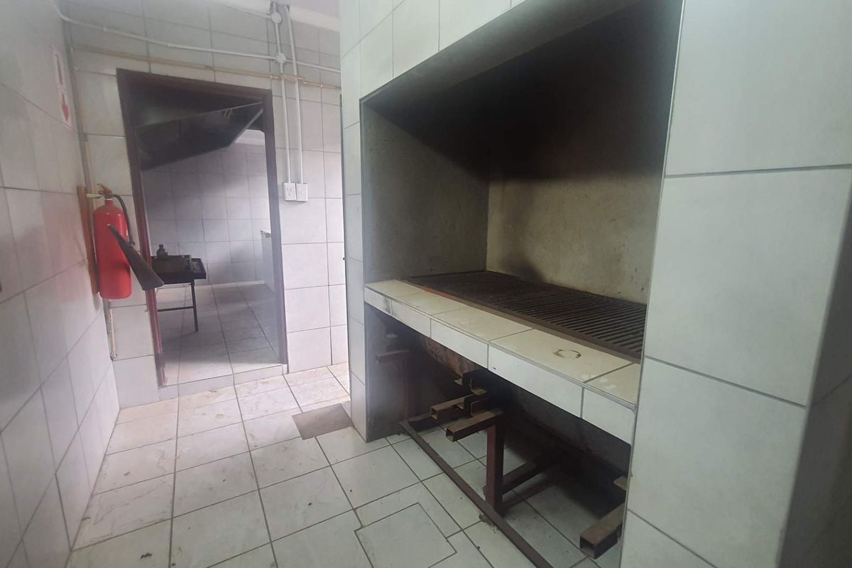 Commercial kitchen area featuring a built-in braai or grill station with tiled finishes and direct access to an adjacent prep room.