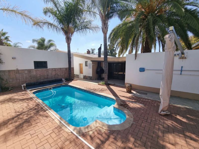Outdoor pool area featuring a swimming pool, brick paving, built-in braai, and established palm trees within a private courtyard setting.