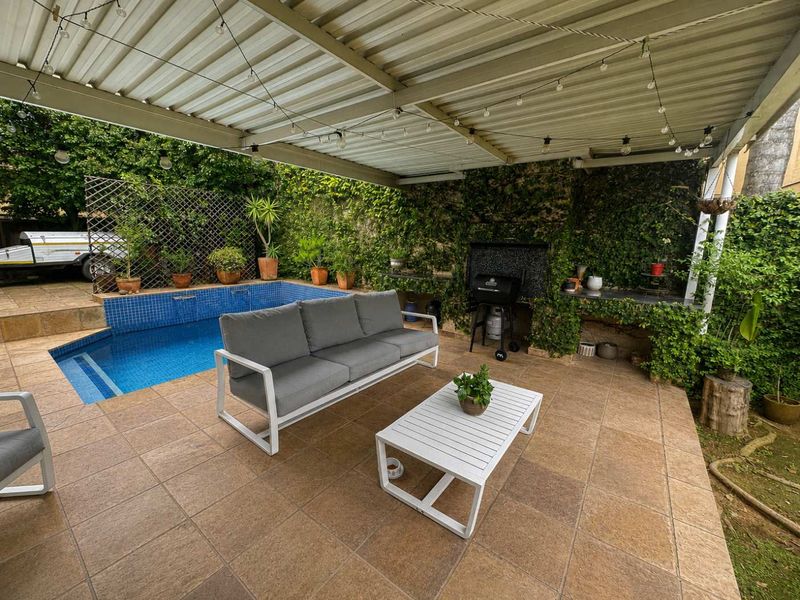 Covered outdoor patio area featuring a built-in braai, tiled flooring, and direct access to a swimming pool.