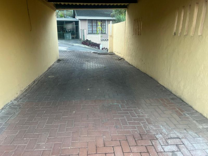 A covered carport area featuring paved flooring and side retaining walls, providing sheltered off-street parking.