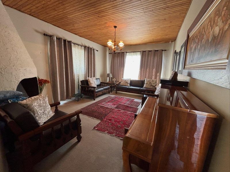 A traditional living room featuring a warm timber-clad ceiling, carpeted flooring, and a built-in fireplace, offering a cozy and classic atmosphere.