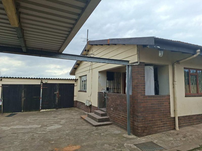 Front exterior view of the house featuring a concrete driveway, attached carport, and brick facade with security features.