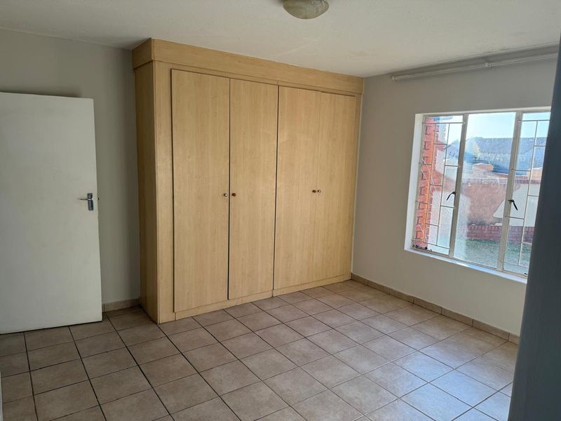 A vacant bedroom featuring built-in wooden cupboards, tiled flooring, and a window with security bars.