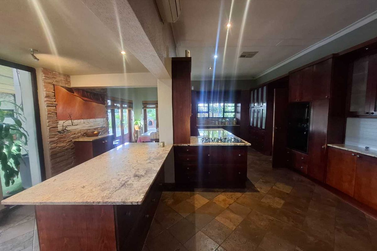 Spacious kitchen featuring dark wood cabinetry, granite countertops, a central island with a built-in gas hob, and natural stone floor tiles.