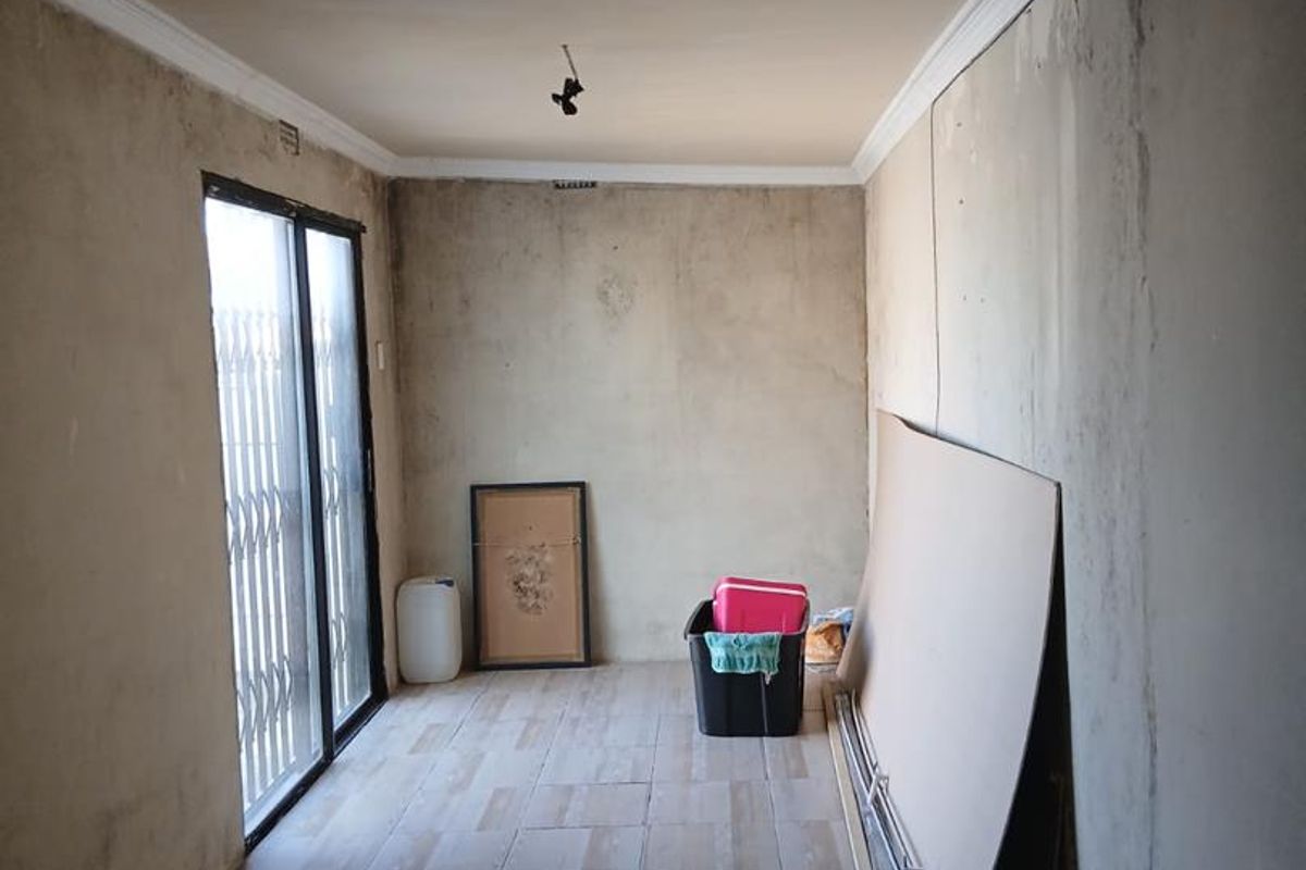 An empty, unfinished living area featuring tiled flooring, crown molding, and a sliding glass door with a security gate.