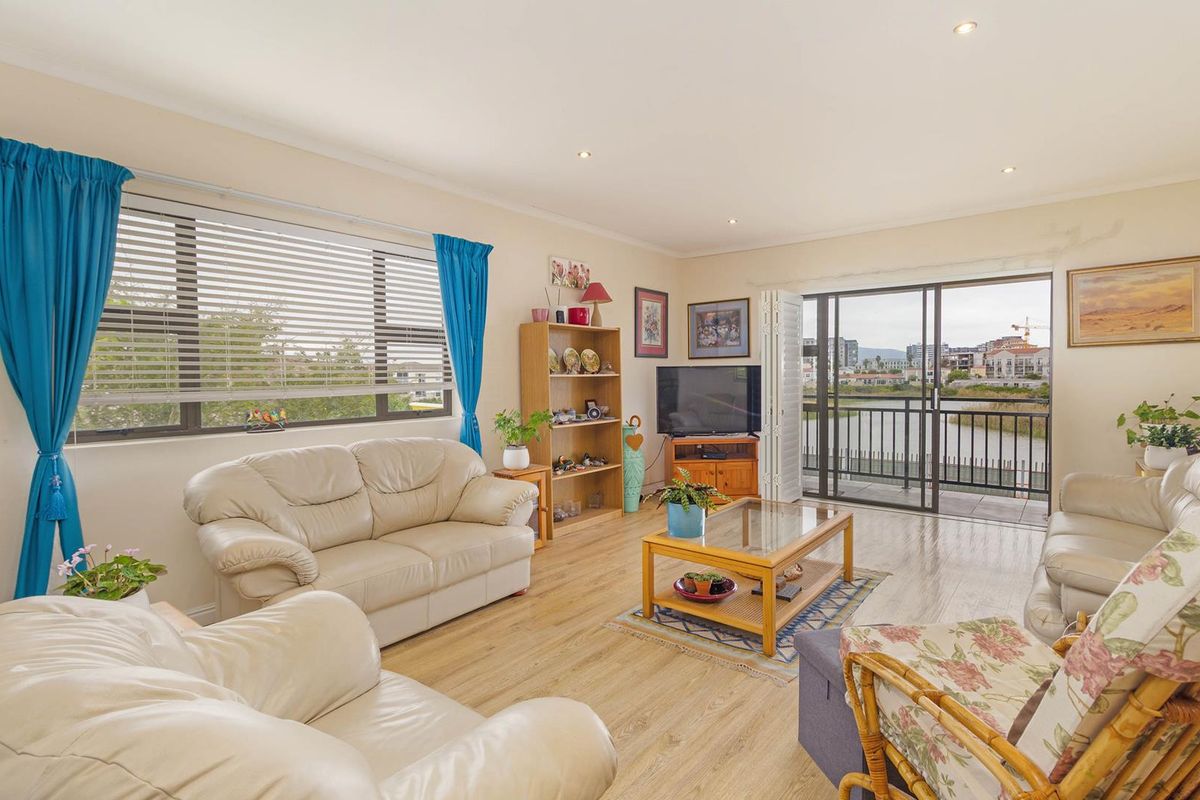 Spacious living room featuring laminate flooring, recessed lighting, and large sliding glass doors opening onto a balcony with scenic water views.