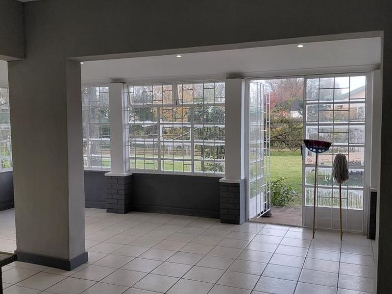 Spacious, light-filled living area featuring neutral tiled flooring, recessed lighting, and large grid-pattern windows with direct access to the garden.