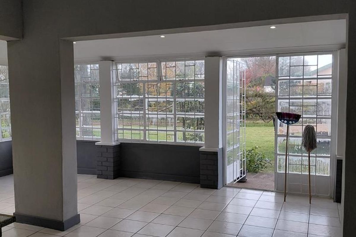 Spacious, light-filled living area featuring neutral tiled flooring, recessed lighting, and large grid-pattern windows with direct access to the garden.