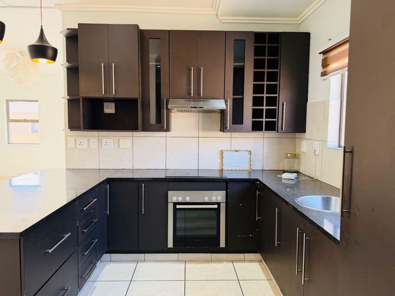 Modern U-shaped kitchen featuring dark wood cabinetry, granite countertops, built-in oven, electric hob, and a tiled backsplash.
