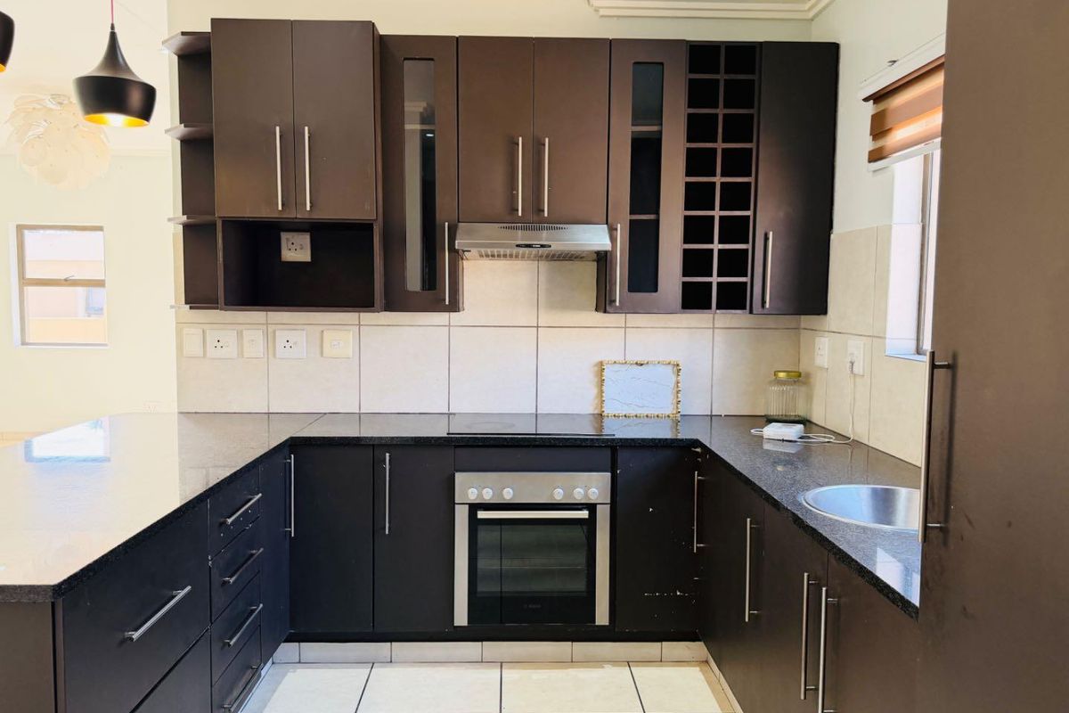 Modern U-shaped kitchen featuring dark wood cabinetry, granite countertops, built-in oven, electric hob, and a tiled backsplash.