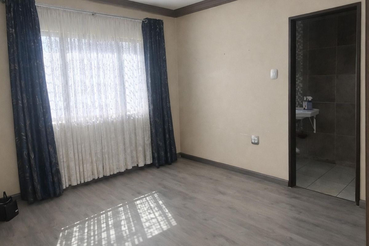 A clean, empty bedroom featuring modern laminate flooring, crown molding, and direct access to an en-suite bathroom.