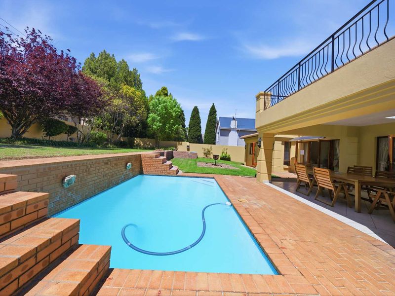 Outdoor pool area featuring a swimming pool, brick retaining wall, and a covered patio space with access to the upper balcony.