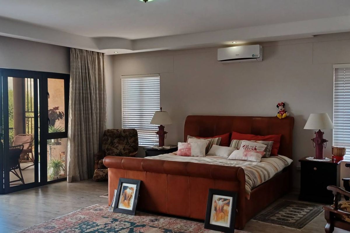 Spacious bedroom featuring recessed ceiling lighting, split-system air conditioning, and large sliding glass doors opening onto a private balcony with scenic views.