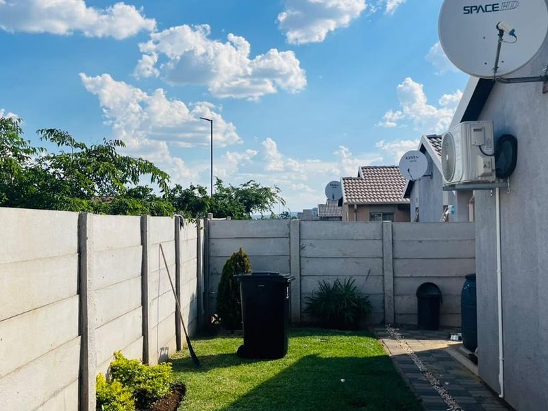 A rear garden area featuring a precast concrete boundary wall, a paved walkway, and an exterior air conditioning unit mounted to the house wall.