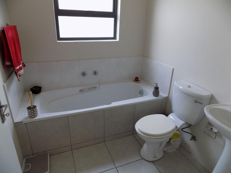 A functional bathroom featuring a built-in bathtub with tiled surround, a pedestal sink, and a standard flush toilet with neutral floor tiling.