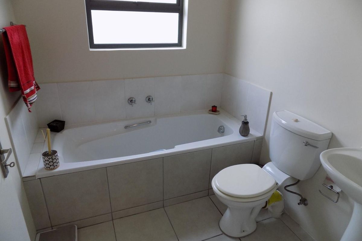 A functional bathroom featuring a built-in bathtub with tiled surround, a pedestal sink, and a standard flush toilet with neutral floor tiling.