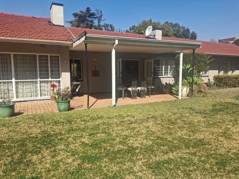 Rear view of the house featuring a covered patio area with brick paving, overlooking a garden with a lawn.