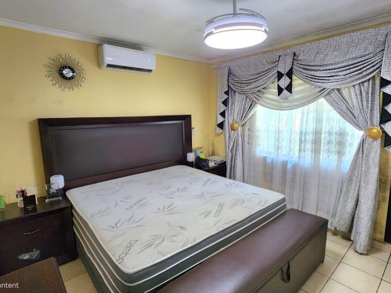 A bedroom featuring tiled flooring and a wall-mounted split-system air conditioner. The space requires cosmetic updates to the wall finishes.