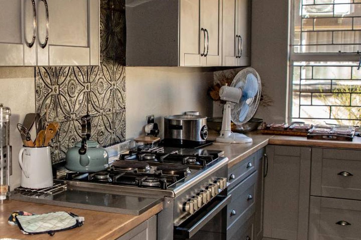 A well-appointed kitchen featuring grey cabinetry, wooden countertops, a gas stove with extractor fan, and decorative tiled backsplash.