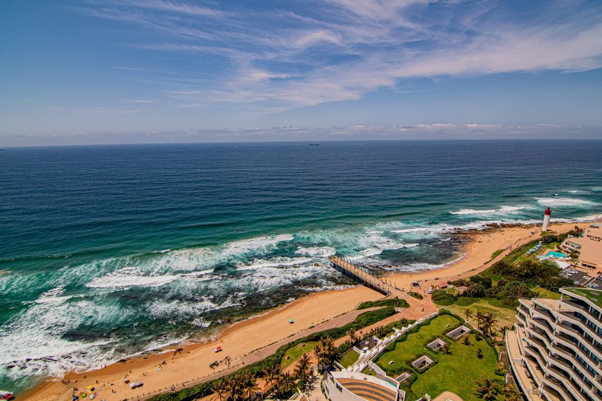 An elevated aerial view showcasing the coastline, sandy beach, pier, and surrounding coastal landscape from the penthouse perspective.