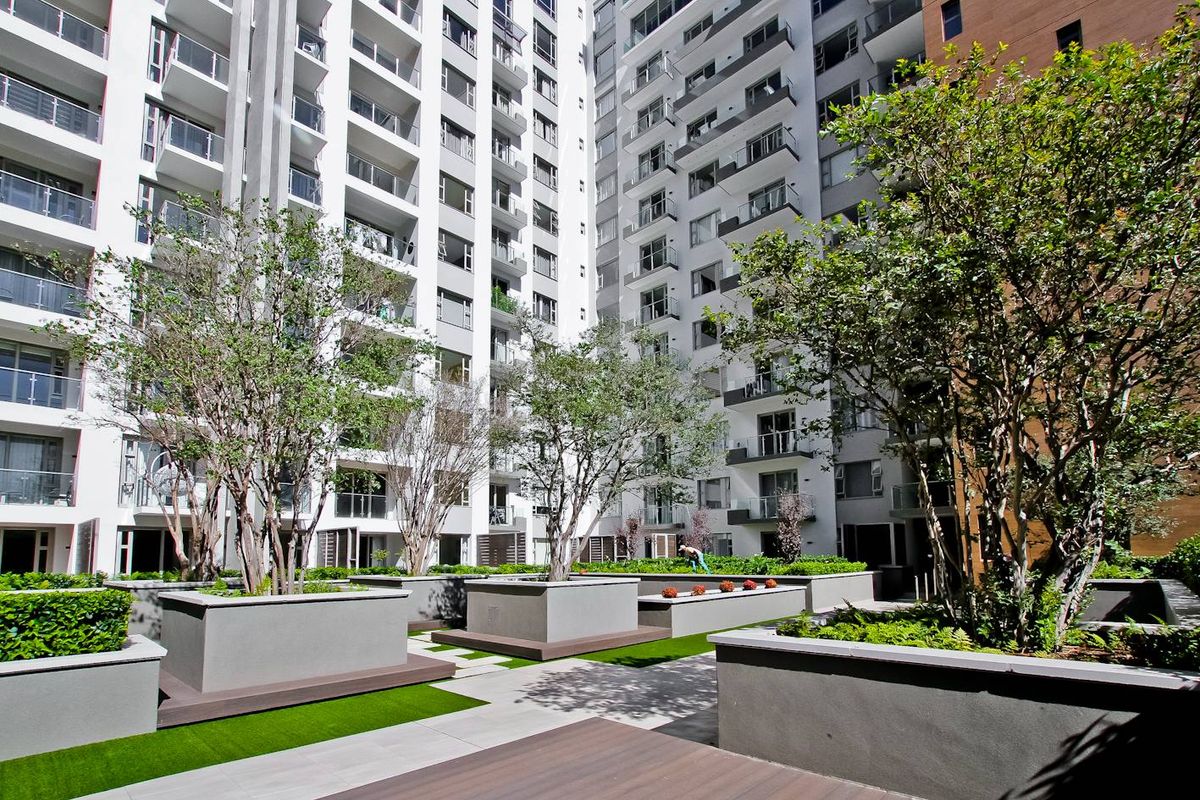 A well-maintained communal courtyard area featuring raised concrete planters, paved pathways, and artificial turf, surrounded by the apartment building facade.