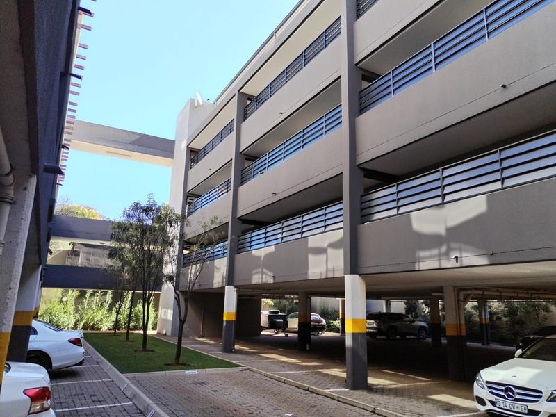 Exterior view of a modern apartment complex featuring multi-level balconies, covered ground-floor parking, and paved driveway access.