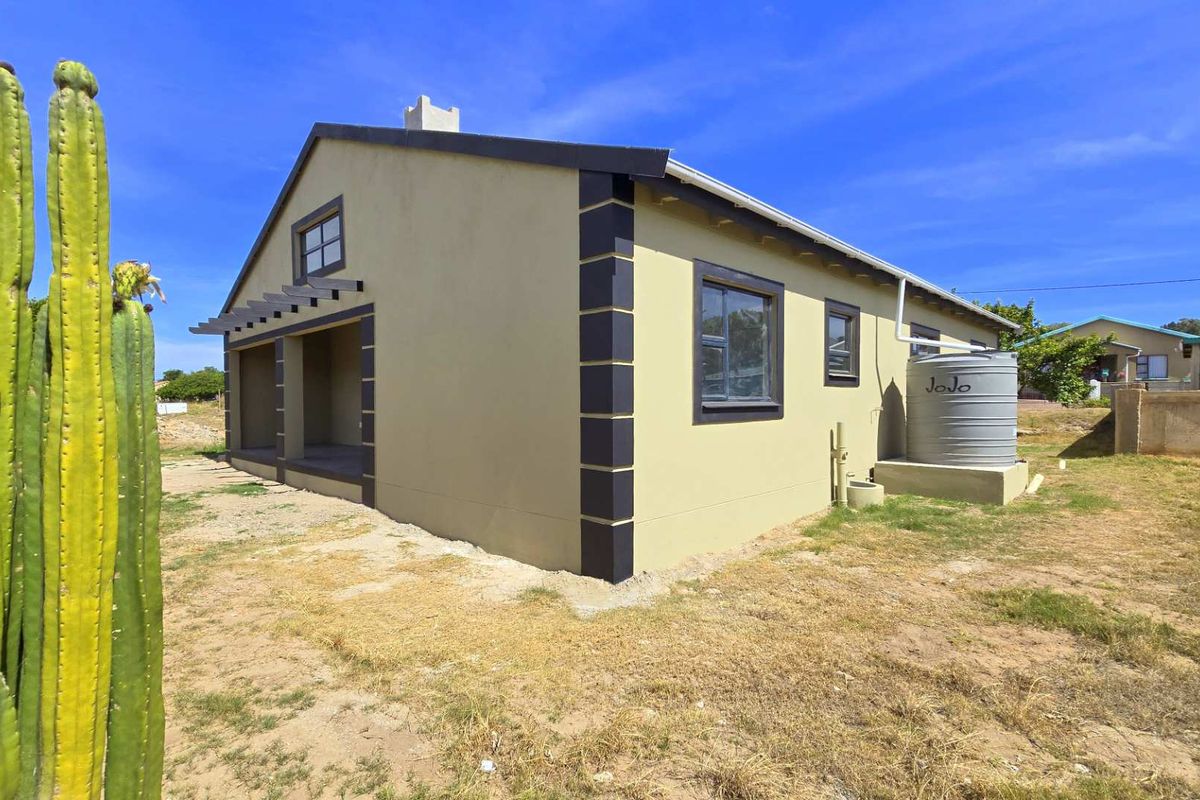 Side view of the house featuring a covered patio area, exterior water storage tank, and painted masonry finish with contrasting corner detailing.
