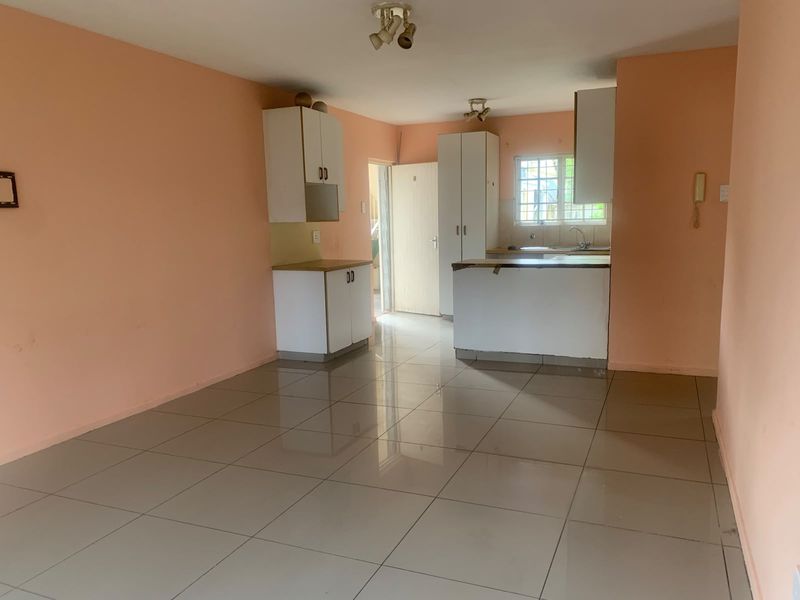 An open-plan living and kitchen area featuring tiled flooring, white cabinetry, and a functional kitchen layout, presenting a blank canvas for potential updates.