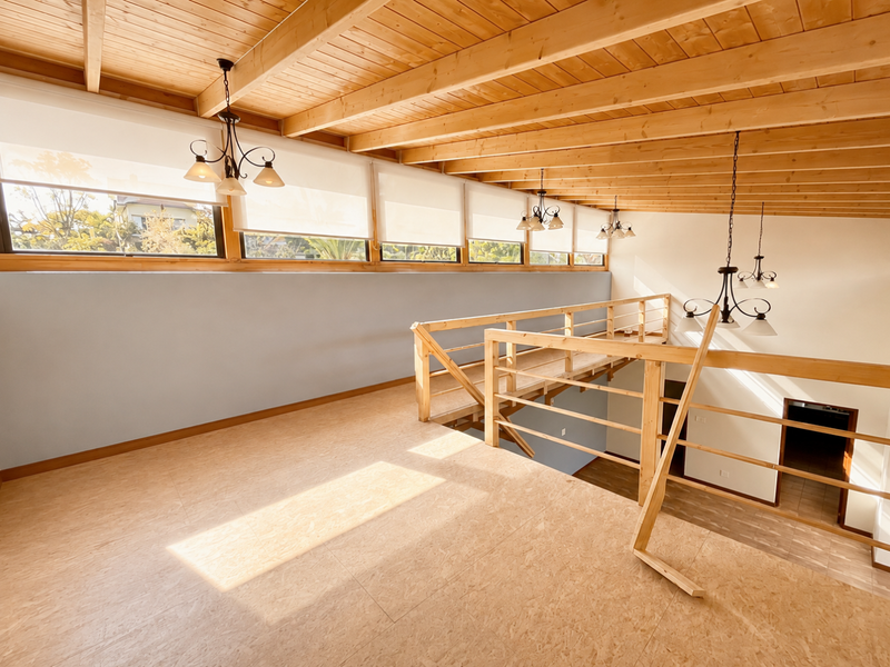 Spacious mezzanine living area featuring exposed timber beam ceilings, natural light, and a timber staircase overlooking the lower level.