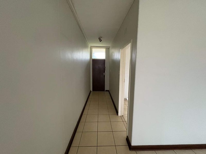 A clean, empty hallway featuring neutral tiled flooring and a direct entrance door, providing a simple transition space within the apartment.