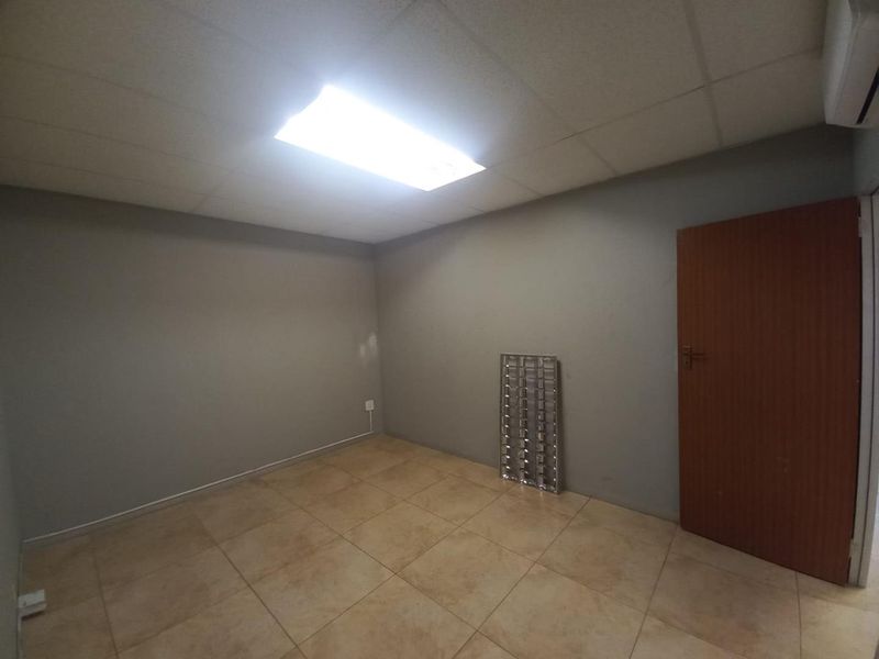 A vacant office space featuring ceramic floor tiles, a drop ceiling with recessed lighting, and an integrated air conditioning unit.