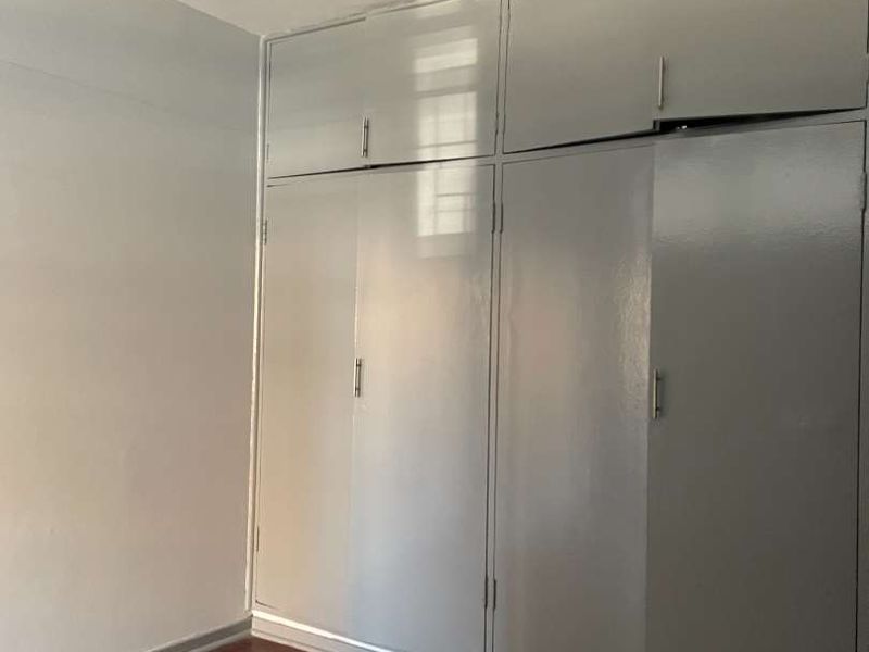 A bedroom featuring classic parquet flooring and extensive floor-to-ceiling built-in cupboards with a neutral grey finish.