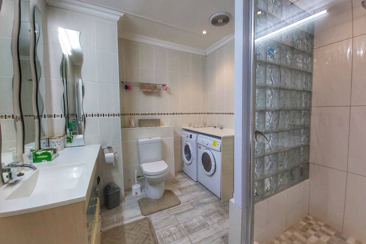 A combined bathroom and laundry area featuring a glass block shower enclosure, vanity basin, toilet, and integrated laundry appliances.