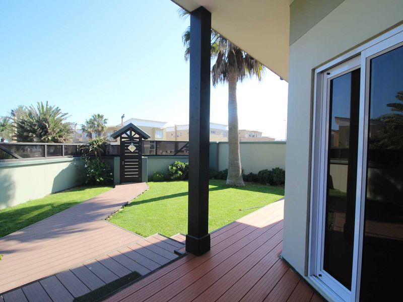 A covered patio featuring composite decking, a sliding glass door, and a well-maintained garden with a private pedestrian gate and boundary wall.