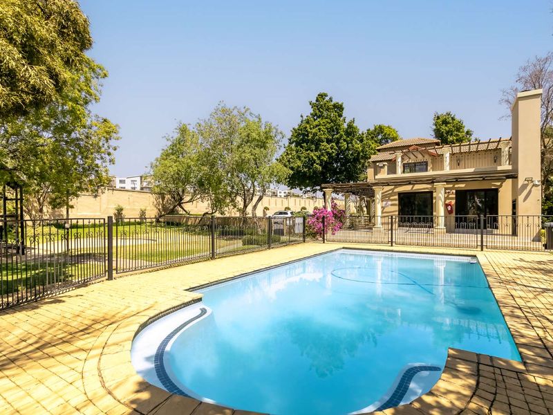 A well-maintained swimming pool area featuring a paved deck, wrought iron safety fencing, and a covered patio area attached to the main residence.