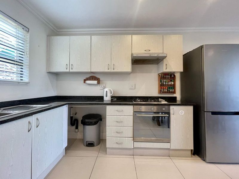 Functional kitchen featuring light-toned laminate cabinetry, granite countertops, built-in oven with gas hob, and tiled flooring.