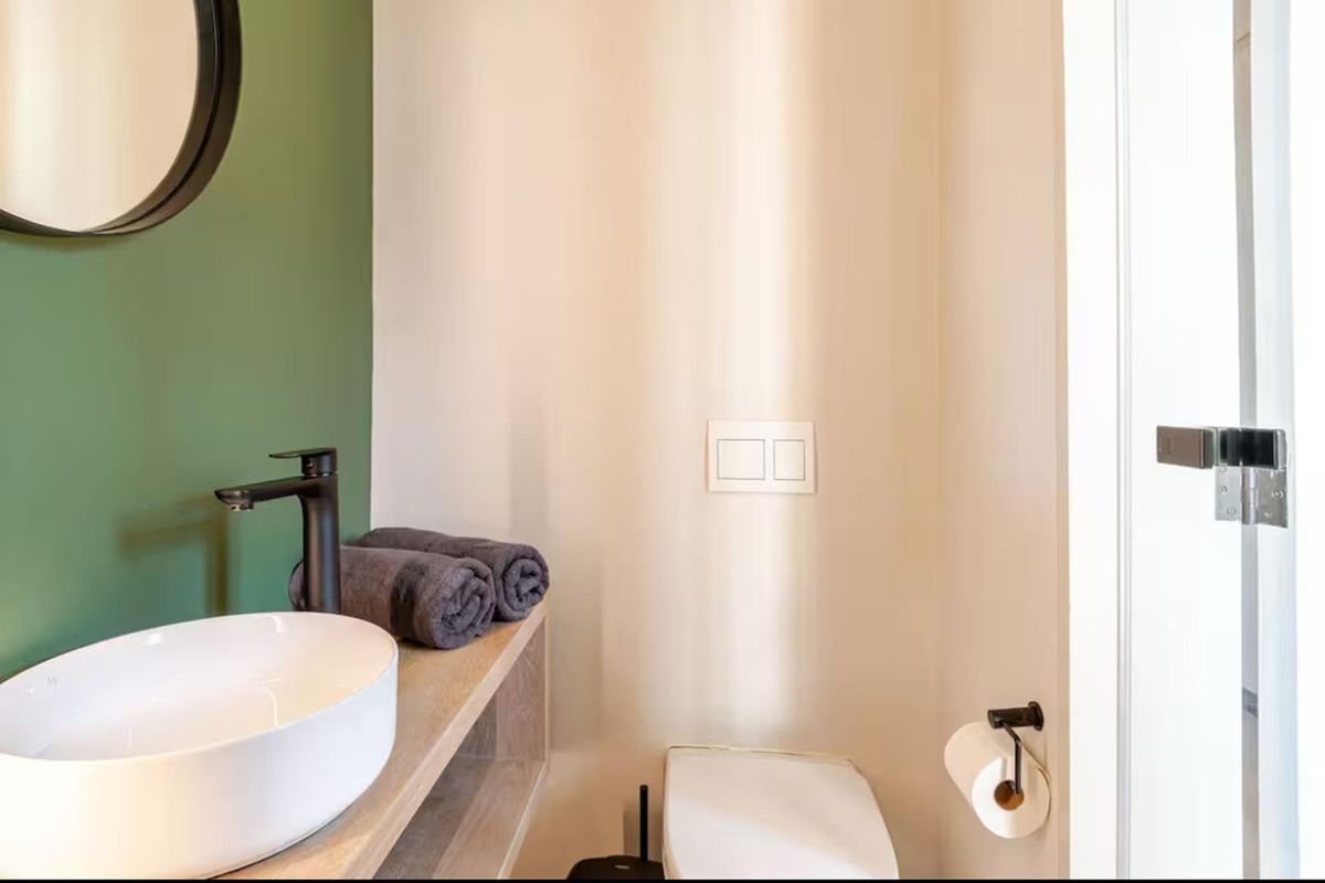 A modern powder room featuring a contemporary vessel sink, matte black faucet, wall-mounted toilet, and a stylish green accent wall.