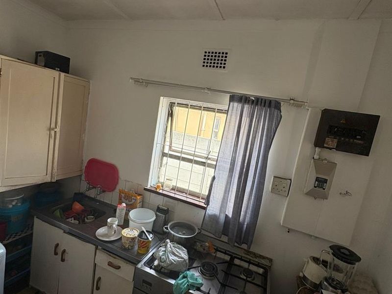 A compact, dated kitchen featuring basic cabinetry, a gas stove with oven, and a window with security bars.