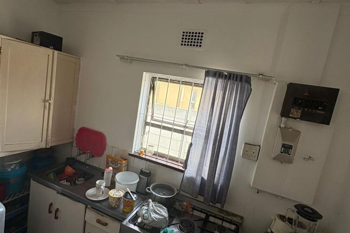 A compact, dated kitchen featuring basic cabinetry, a gas stove with oven, and a window with security bars.