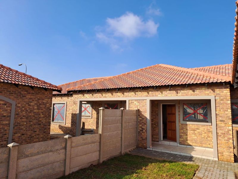 Rear view of a face brick townhouse featuring a tiled roof, paved walkway, and a private garden area with precast concrete boundary walls.