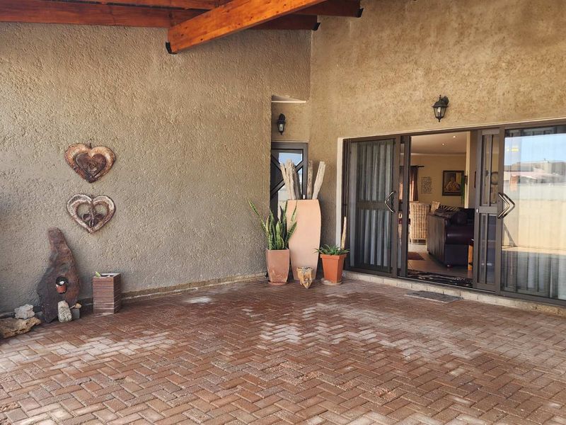 A covered patio area featuring brick paver flooring, exposed timber beams, and sliding glass doors providing access to the interior living space.