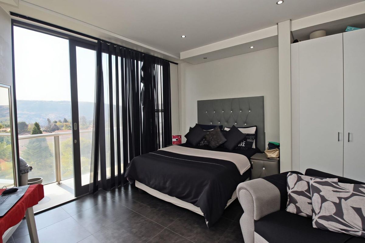 Modern bedroom featuring tiled flooring, built-in cupboards, recessed ceiling lighting, and large sliding glass doors opening onto a private balcony with scenic views.