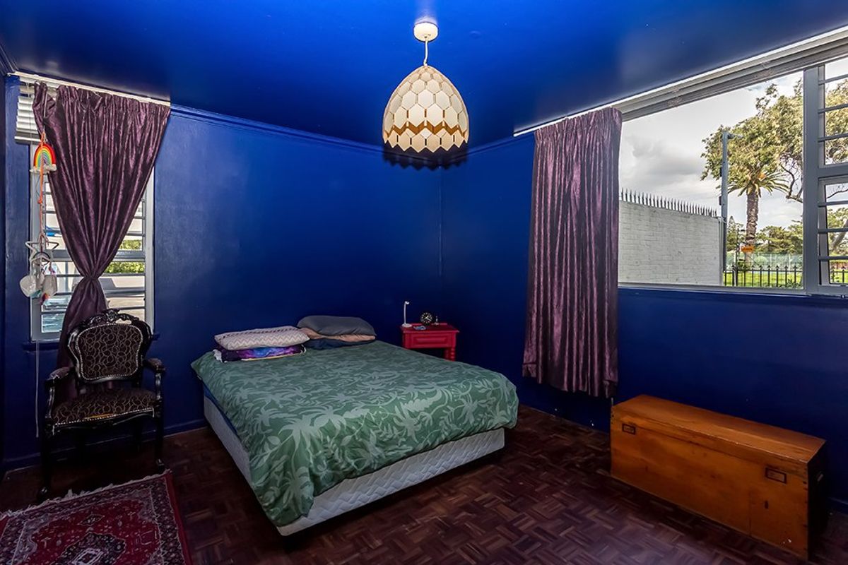 A bedroom featuring dark blue walls, parquet flooring, and large windows providing natural light.